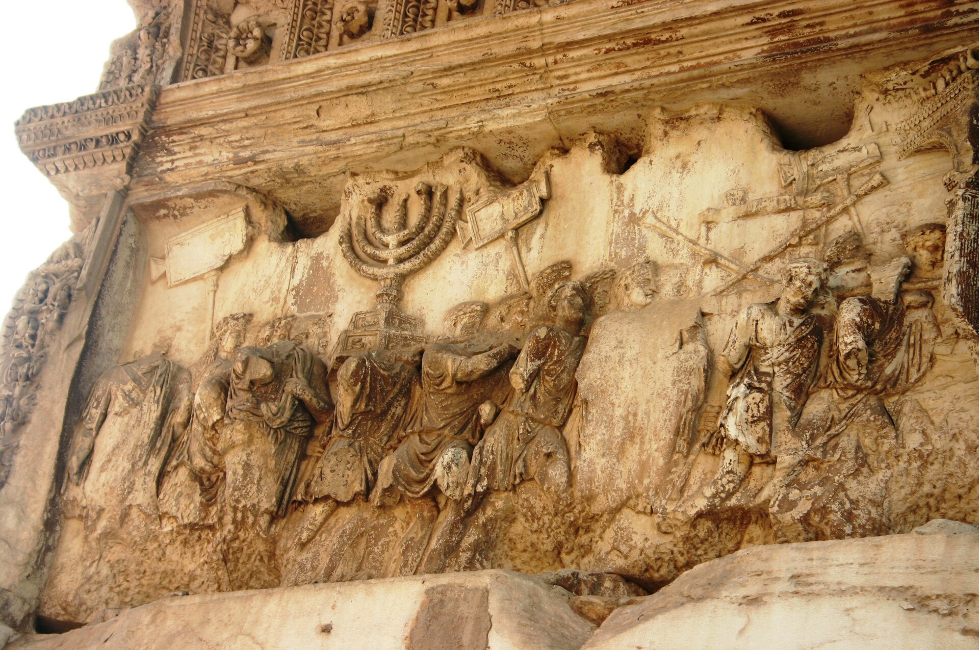 Relevo de pedra desgastado com figuras em procissão carregando um grande candelabro de sete braços.