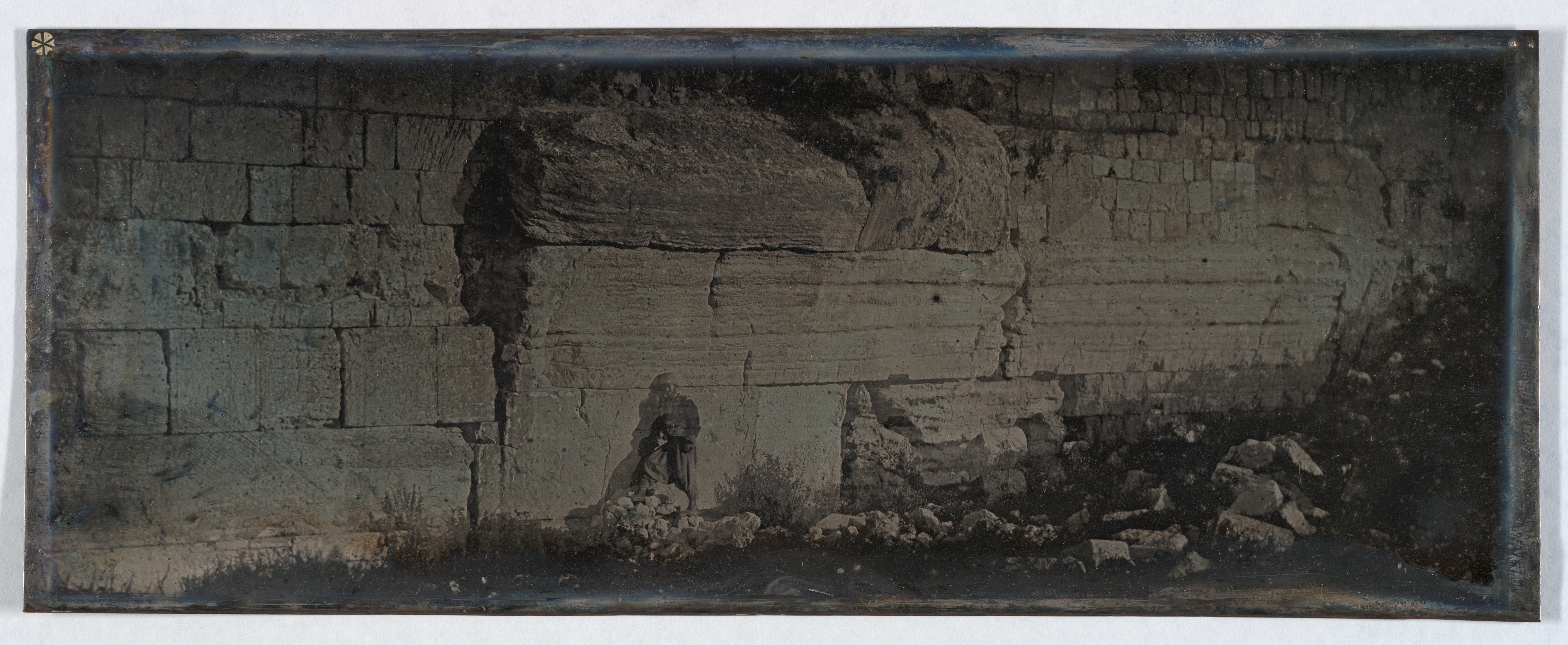 Fotografia antiga em tons sépia do muro ocidental do Monte do Templo, com a pedra saliente do Arco de Robinson.